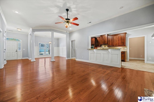 unfurnished living room featuring ornate columns, wood-type flooring, crown molding, and ceiling fan