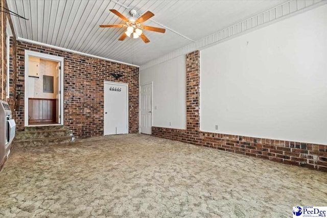carpeted empty room with ceiling fan and brick wall