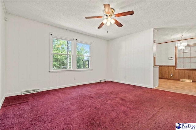 spare room featuring wood walls, visible vents, a textured ceiling, and ceiling fan with notable chandelier