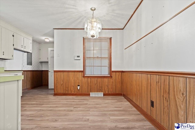 unfurnished dining area featuring light wood-style flooring, wood walls, visible vents, wainscoting, and a chandelier