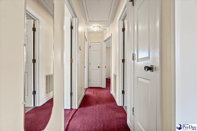hall with baseboards, dark carpet, attic access, and visible vents