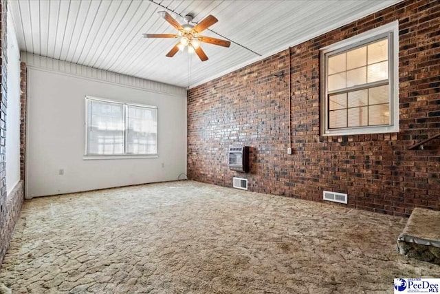 carpeted empty room with brick wall, ceiling fan, heating unit, and visible vents