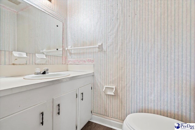 bathroom with vanity, toilet, wallpapered walls, and wood finished floors