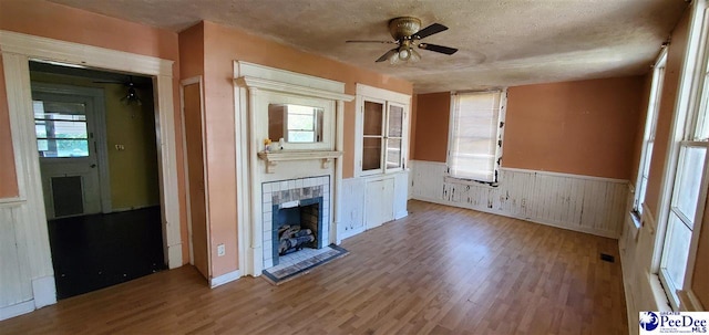 unfurnished living room with ceiling fan, a tiled fireplace, hardwood / wood-style floors, and a textured ceiling