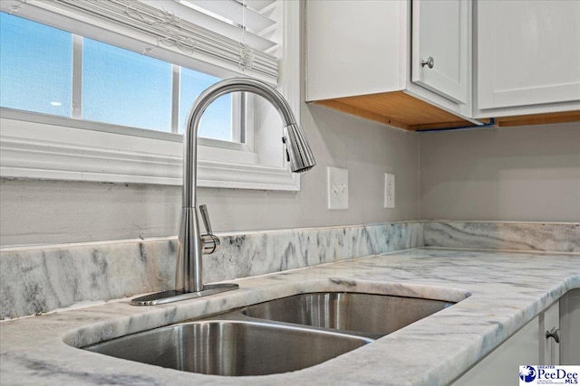 details featuring light stone countertops, white cabinets, and a sink