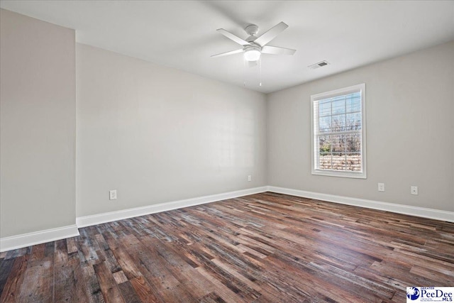 spare room with dark wood-style flooring, visible vents, and baseboards