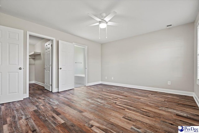 unfurnished bedroom featuring a walk in closet, dark wood-style flooring, visible vents, a ceiling fan, and baseboards