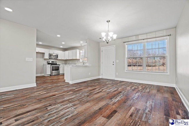 unfurnished living room featuring baseboards, dark wood-type flooring, recessed lighting, and an inviting chandelier