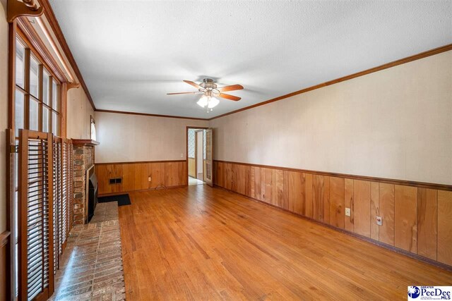 3116 Kenfield Ln, Florence, SC 29505 - unfurnished living room with wood finished floors, a wainscoted wall, a ceiling fan, wooden walls, and a brick fireplace