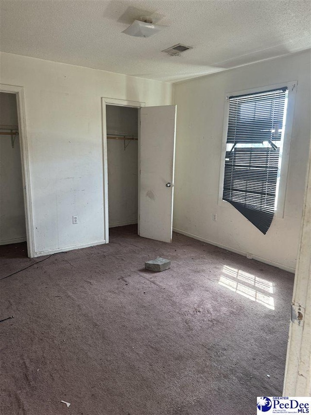 unfurnished bedroom featuring multiple windows, carpet flooring, two closets, and a textured ceiling