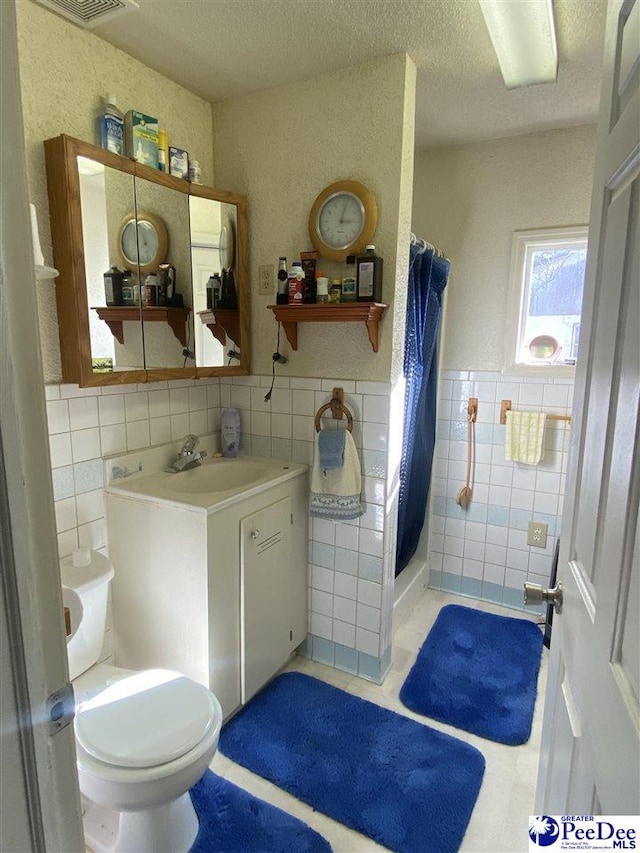 bathroom with tile walls, vanity, walk in shower, toilet, and a textured ceiling