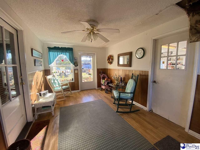 sitting room featuring hardwood / wood-style floors, wooden walls, a textured ceiling, and ceiling fan