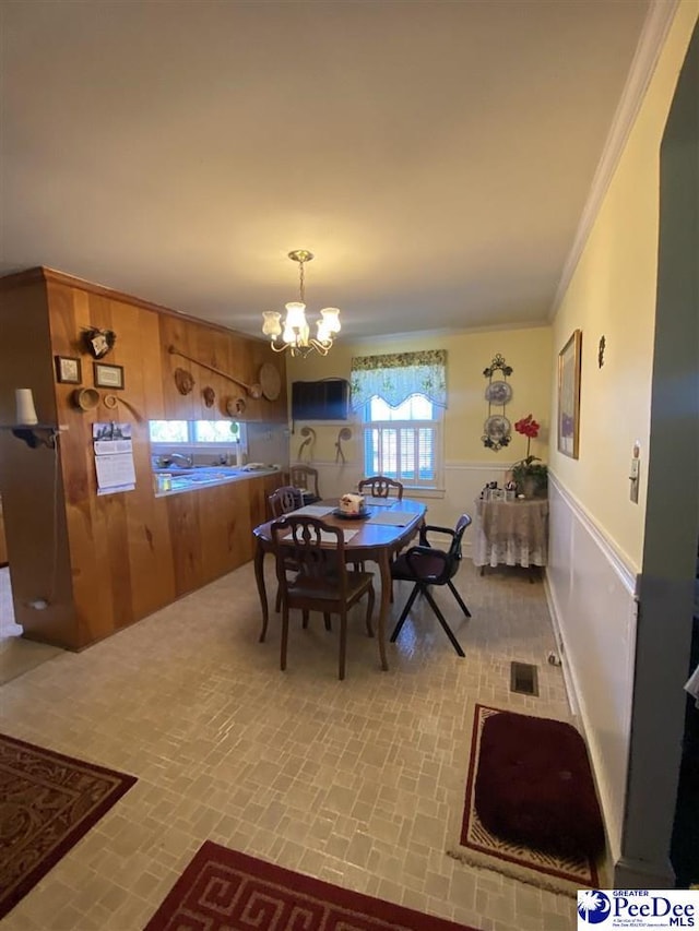 dining space with ornamental molding, an inviting chandelier, and wood walls