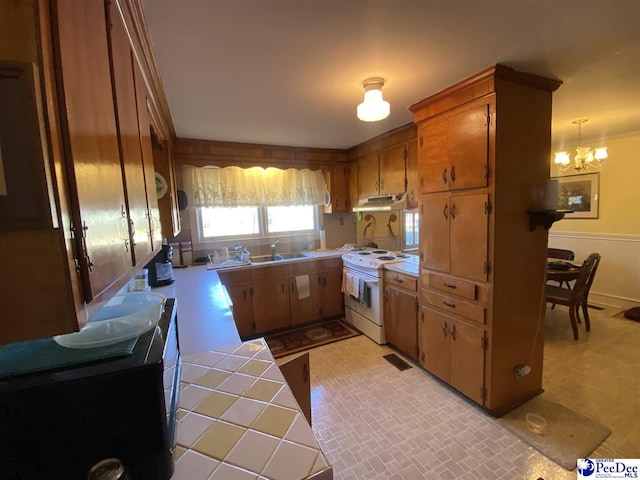 kitchen with electric stove, sink, a notable chandelier, and tile countertops