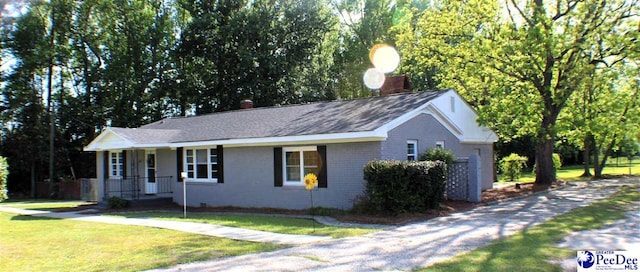 ranch-style home featuring covered porch, a chimney, a front lawn, and brick siding