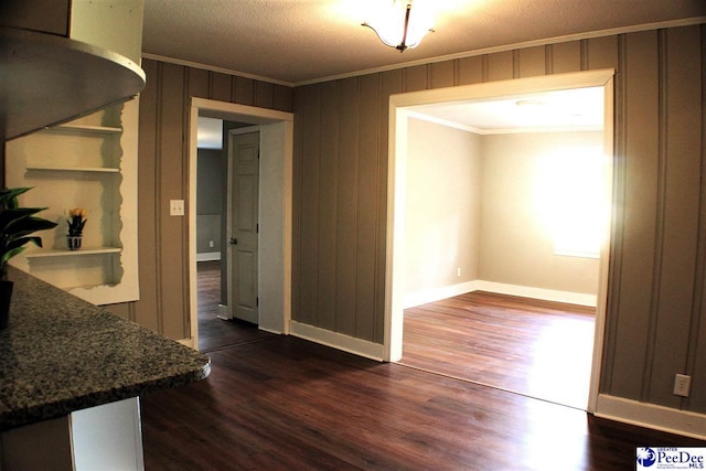 unfurnished dining area with dark wood-type flooring, ornamental molding, baseboards, and wooden walls