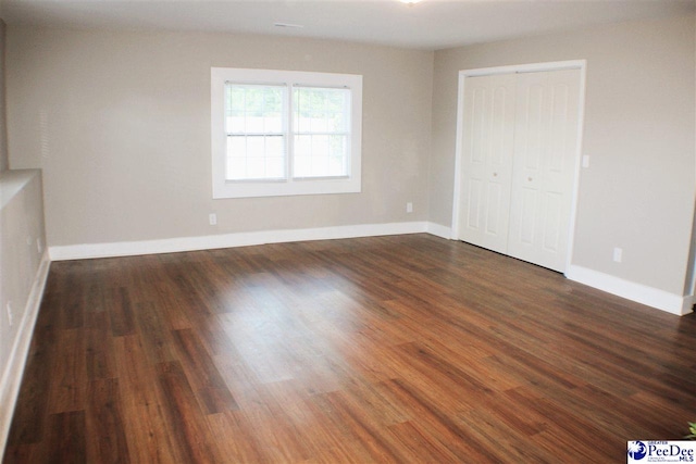 unfurnished living room featuring baseboards and dark wood-style flooring