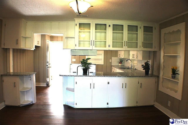 kitchen with dark wood-style flooring, open shelves, a sink, dark stone counters, and a peninsula