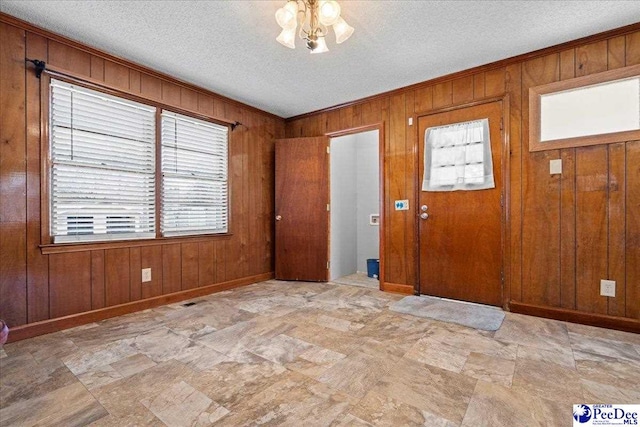 foyer with crown molding, wooden walls, and a textured ceiling