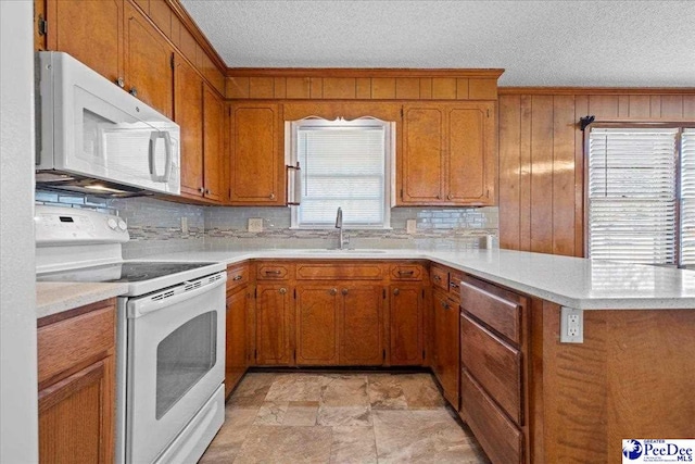 kitchen with light countertops, brown cabinets, a peninsula, white appliances, and a sink