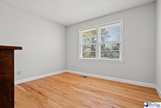 unfurnished room featuring wood finished floors, visible vents, and baseboards