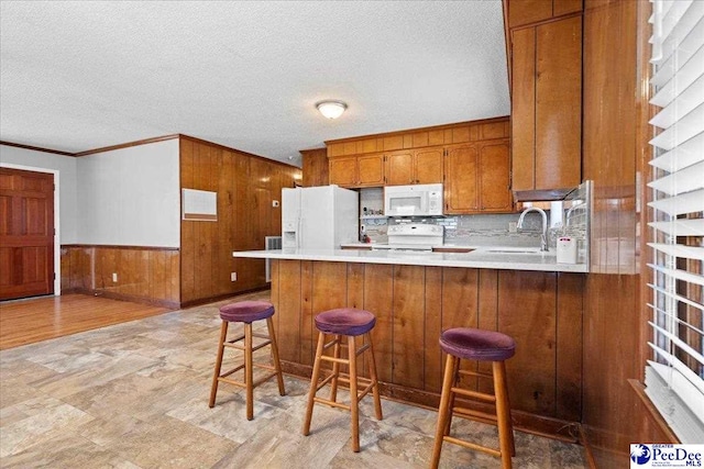 kitchen with wooden walls, brown cabinets, a peninsula, white appliances, and a sink