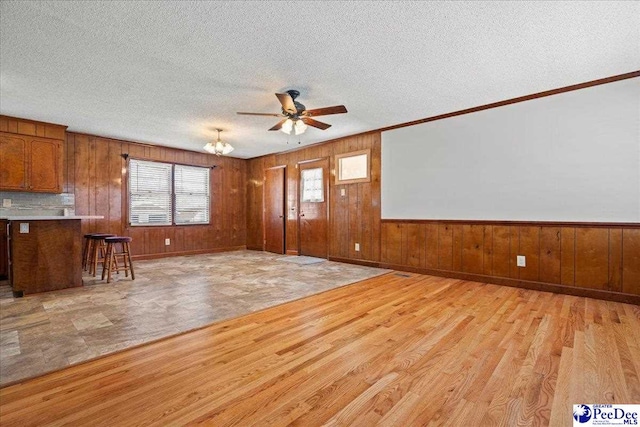 interior space with light wood-style floors, wooden walls, and ceiling fan with notable chandelier