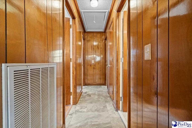 corridor with attic access, wood walls, crown molding, and a heating unit