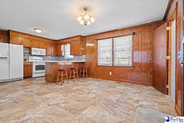 kitchen with white appliances, wooden walls, brown cabinetry, a peninsula, and light countertops