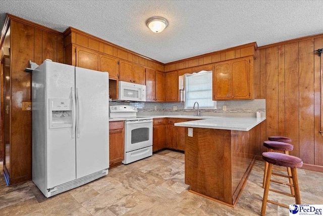 kitchen featuring wooden walls, light countertops, brown cabinets, a peninsula, and white appliances