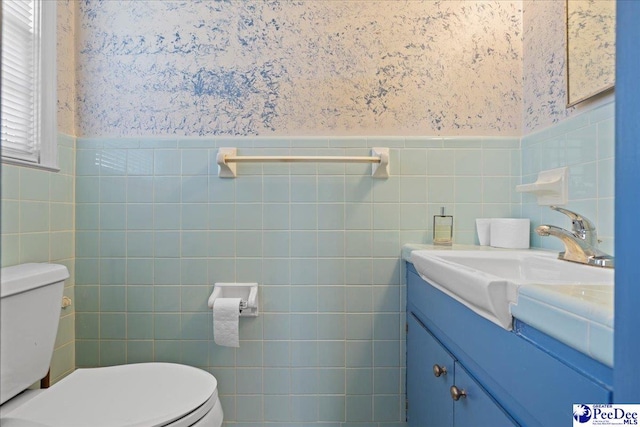 bathroom with wallpapered walls, toilet, vanity, and wainscoting