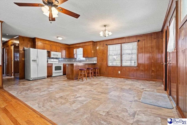 kitchen featuring brown cabinets, open floor plan, white appliances, a peninsula, and wood walls