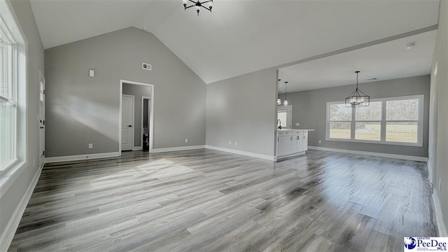 unfurnished living room with high vaulted ceiling, a chandelier, and light hardwood / wood-style floors