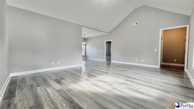 empty room with a notable chandelier, light hardwood / wood-style flooring, and high vaulted ceiling