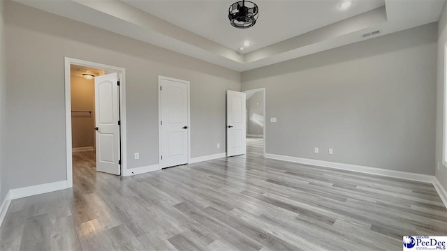 unfurnished bedroom with a raised ceiling and light hardwood / wood-style floors