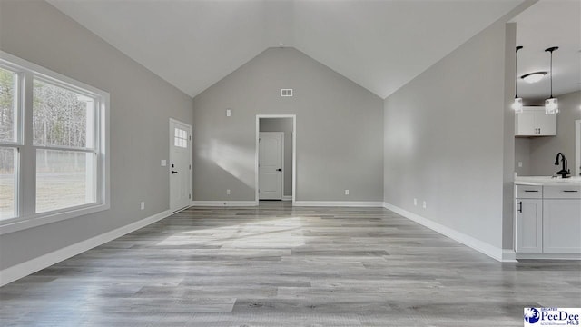 unfurnished living room with high vaulted ceiling, sink, and light hardwood / wood-style floors