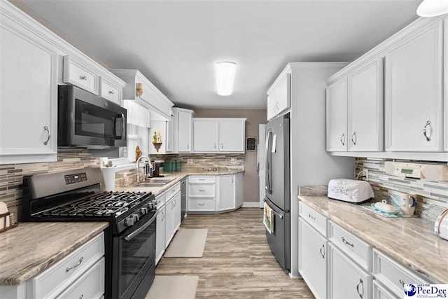 kitchen with appliances with stainless steel finishes, white cabinetry, sink, backsplash, and light hardwood / wood-style floors