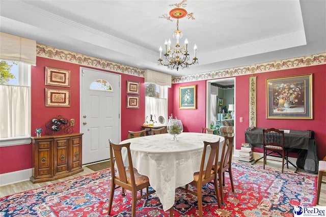 dining area with a tray ceiling, ornamental molding, a chandelier, and light wood-type flooring