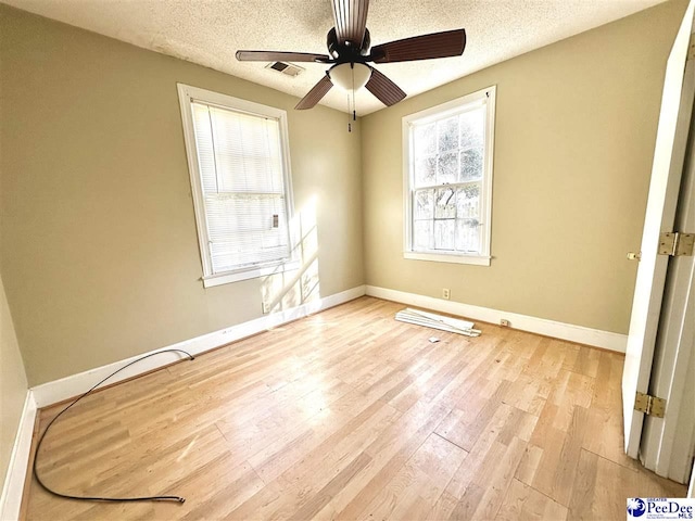 empty room featuring light wood finished floors, baseboards, and a textured ceiling