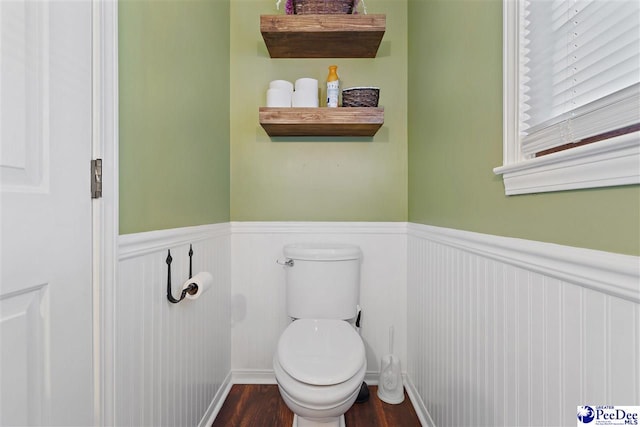 bathroom with a wainscoted wall, wood finished floors, and toilet