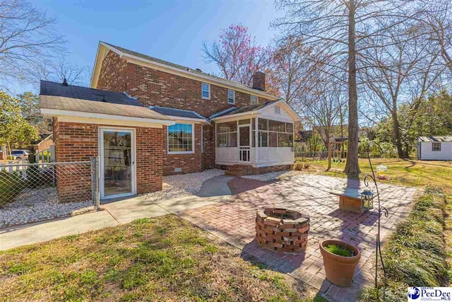 rear view of house featuring brick siding, a patio, a chimney, an outdoor fire pit, and a sunroom