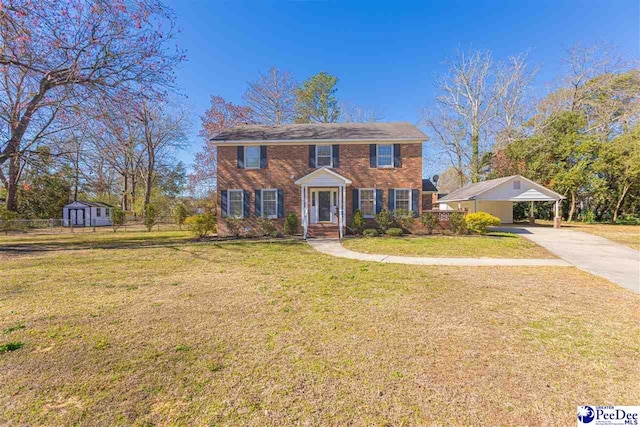 colonial home with concrete driveway, an outbuilding, a shed, a front lawn, and a carport