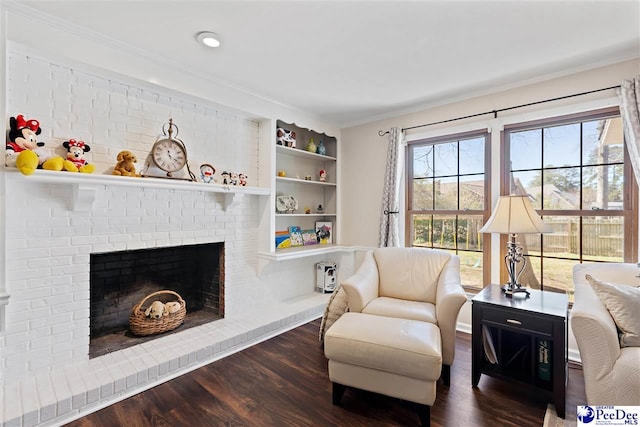 sitting room with a brick fireplace, crown molding, and wood finished floors