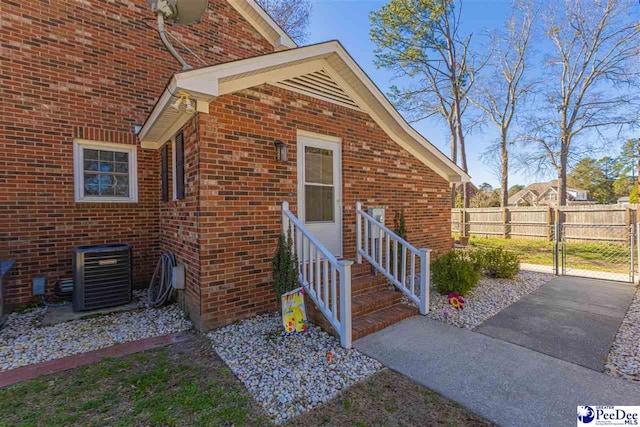 property entrance featuring a gate, brick siding, fence, and central AC unit