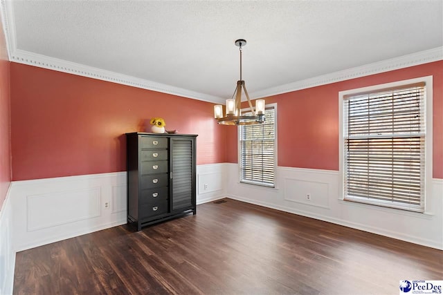 unfurnished dining area with dark wood-style floors, a wainscoted wall, a notable chandelier, and a textured ceiling