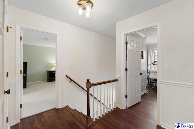 corridor with a textured ceiling, wood finished floors, and an upstairs landing