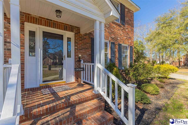 entrance to property with a porch and brick siding