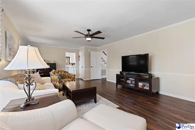 living room with a ceiling fan, wainscoting, ornamental molding, wood finished floors, and stairs