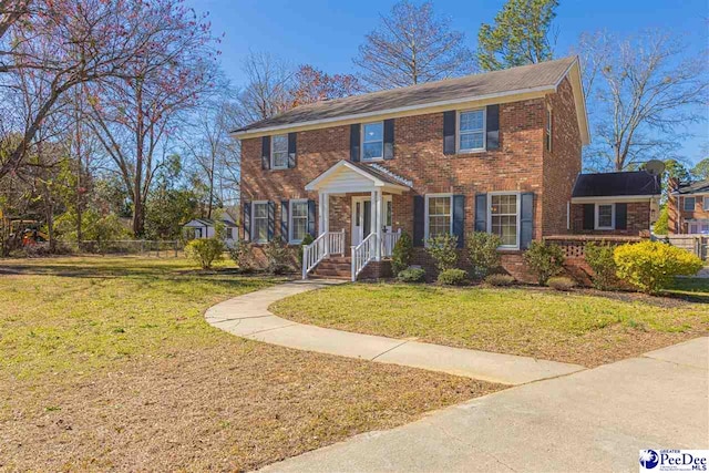 colonial home with fence, a front lawn, and brick siding