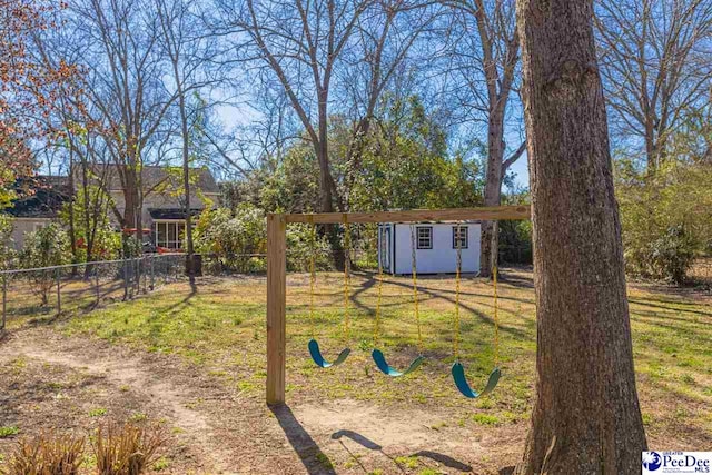 view of yard featuring a storage unit, fence, an outdoor structure, a playground, and a carport